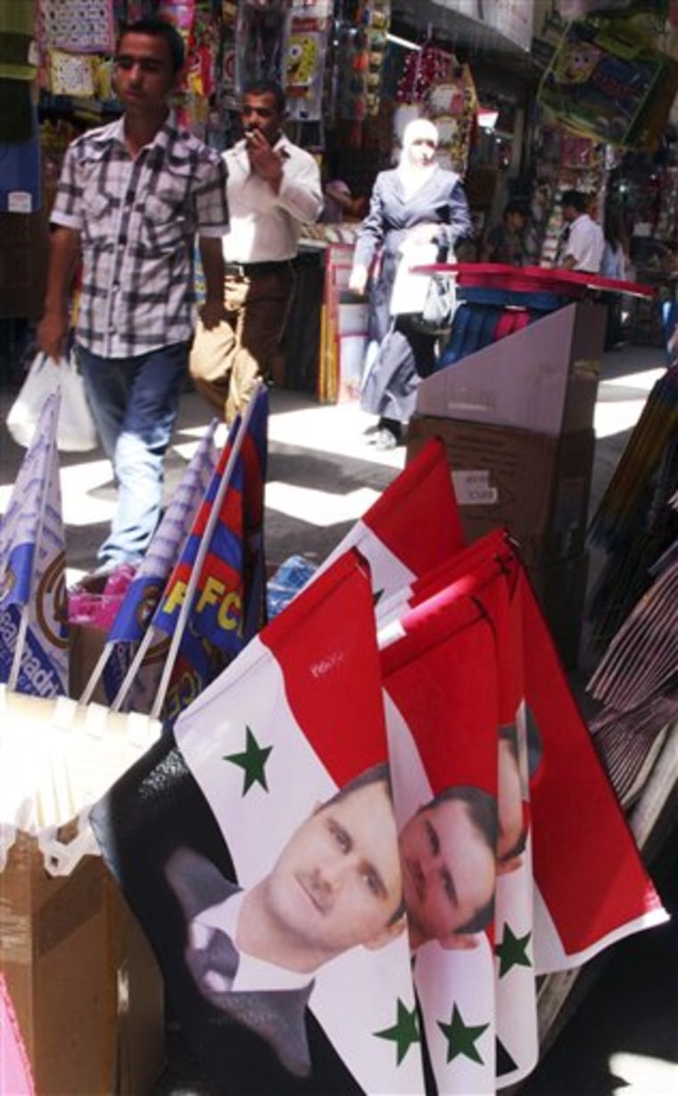 Syrians pass flags with portraits of Syrian President Bashar Assad at a popular market in downtown Damascus on Monday.